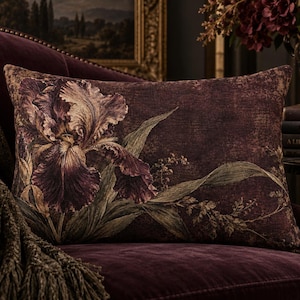 Puede incluir: Un cojín rectangular con un estampado botánico detallado de una gran flor de iris de color púrpura oscuro con follaje verde sobre un fondo granate profundo y texturizado. La tela tiene una apariencia tejida con tonos ricos y detalles florales.