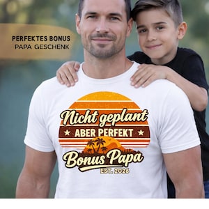 Könnte beinhalten: Weißes T-Shirt mit Retro-Sonnenuntergangsdesign und dem Text "Nicht geplant aber Perfekt Bonus Papa EST. 2026". Ein Mann trägt das Shirt, mit den Armen eines Jungen um seine Schultern. Der Text "PERFEKTES BONUS PAPA GESCHENK" ist ebenfalls sichtbar.