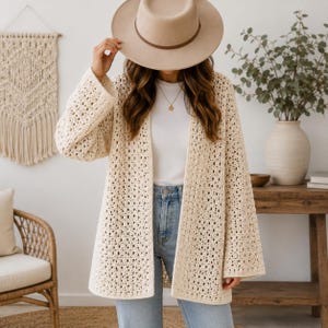 Puede incluir: Un cárdigan de ganchillo color crema abierto por delante, con mangas largas y anchas y un patrón de cuadrados texturizados. La prenda se lleva sobre una camiseta blanca lisa y vaqueros azul claro, junto con un sombrero de fieltro color canela.