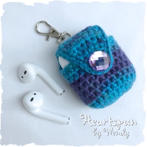 Peut inclure: Une housse en crochet pour écouteurs sans fil avec un design ombré violet et bleu. La housse a un bouton en strass violet et un porte-clés argenté.