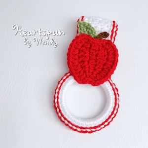 May include: Red and white crocheted pot holder with an apple design. The apple is red with a green leaf and brown stem. The text "Heartspun by Wendy" is visible in the image.
