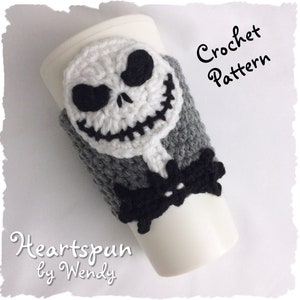 Puede incluir: Patrón de crochet para un calentador de taza de café gris y blanco con una cara de Jack Skellington. El patrón se llama "Heartspun by Wendy".