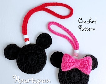 May include: Two crocheted Mickey Mouse characters with red and pink yarn. The characters have black faces and ears. The red character has a white bead on its string. The pink character has a pink bow and a white bead on its string. The text "Crochet Pattern" is written in black on a white background. The text "Heartspun by Wendy" is written in black on a white background.