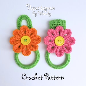 May include: Two handmade crochet towel holders. One has an orange flower with a yellow button centre, the other has a pink flower with a yellow button centre. Both have green loops and green hanging loops. The text "Heartspun by Wendy" and "Crochet Pattern" are visible.