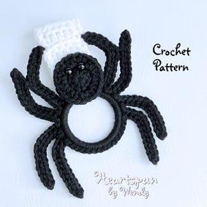 May include: A black crocheted spider with a white crocheted hat. The spider is a ring holder. The text "Crochet Pattern" and "Heartspun by Wendy" is visible in the image.
