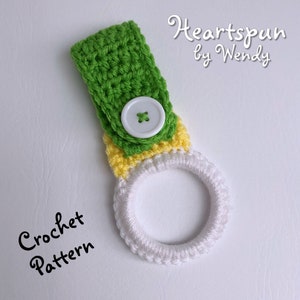 K&ouml;nnte beinhalten: Gr&uuml;ner, gelber und wei&szlig;er geh&auml;kelter Handtuchring mit einem wei&szlig;en Knopf. Der Ring ist mit einer festen Masche geh&auml;kelt und hat einen Knopfverschluss. Der Text "Heartspun by Wendy" und "Crochet Pattern" ist auf dem Bild zu sehen.