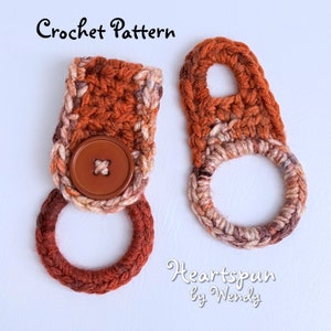 Può includere: Due strofinacci all'uncinetto in tonalità di marrone, arancione e crema. Gli strofinacci hanno un bottone e un anello per appenderli. Il testo "Crochet Pattern" e "Heartspun by Wendy" è visibile nell'immagine.