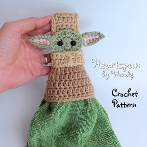 May include: Crochet pattern for a green and brown towel with a crocheted Yoda character on top. The pattern is called "Heartspun by Wendy".