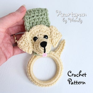 May include: Crochet pattern for a yellow Labrador Retriever dog wearing a green hat. The dog is holding a ring in its mouth. The pattern is called "Heartspun by Wendy".