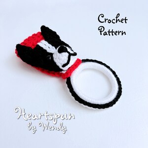 May include: Crochet pattern for a black and white dog head ring holder. The dog has a red collar and is wearing a red hat. The pattern is called "Heartspun by Wendy".