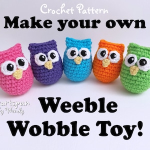 May include: Five crocheted owl toys in different colors: pink, purple, blue, orange, and green. The owls have large black eyes and a yellow beak. The text "Make your own Weeble Wobble Toy!" is below the owls.