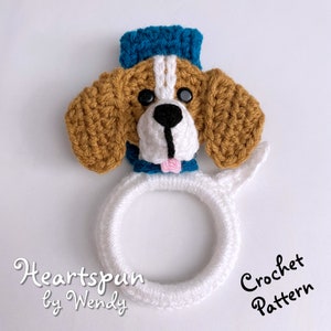 Puede incluir: Patr&oacute;n de crochet para un adorable perro amigurumi con un sombrero azul y un lazo rosa. El patr&oacute;n se llama "Heartspun by Wendy".