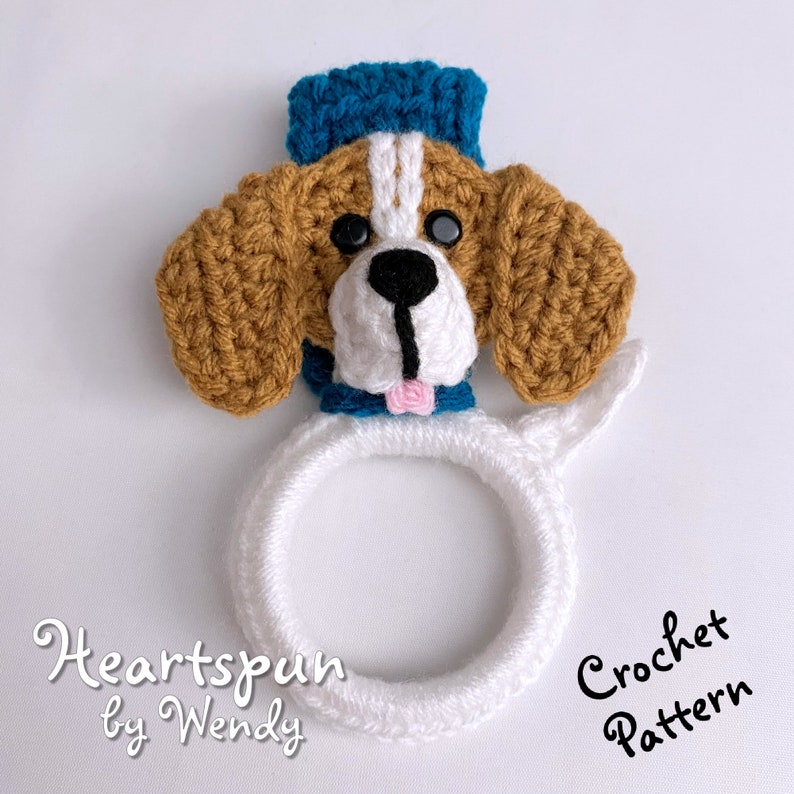 Puede incluir: Patr&oacute;n de crochet para un adorable perro amigurumi con un sombrero azul y un lazo rosa. El patr&oacute;n se llama "Heartspun by Wendy".