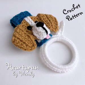 Puede incluir: Patr&oacute;n de crochet para un porta-trapo de cocina con forma de perro. El porta-trapo est&aacute; hecho de hilo blanco y presenta una cabeza de perro de crochet marr&oacute;n y blanco con un sombrero azul. El texto "Crochet Pattern" y "Heartspun by Wendy" es visible en la imagen.