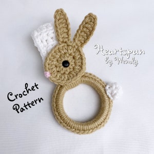 May include: Crochet pattern for a brown bunny ring toy with white accents. The pattern is called "Heartspun by Wendy".
