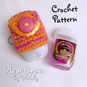 May include: Crochet pattern for a hand sanitizer bottle cover. The cover is made with pink, orange, and yellow yarn and has a pink button. The pattern is called "Heartspun by Wendy".