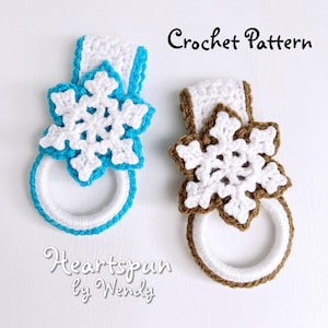 May include: Two crocheted snowflake towel rings. One ring is white with a turquoise border and the other is white with a brown border. The rings are decorated with white crocheted snowflakes. The text "Crochet Pattern" is at the top of the image and the text "Heartspun by Wendy" is at the bottom of the image.