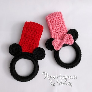 May include: Two crocheted towel holders shaped like Mickey Mouse. One is red and the other is pink. Both have black ears and a black ring for hanging a towel.