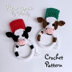 May include: Two crocheted cow-shaped pot holders with black and white spots. One pot holder has a red hat and the other has a green hat. The text "Heartspun by Wendy" and "Crochet Pattern" are visible in the image.