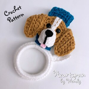 Puede incluir: Patr&oacute;n de crochet para un adorable juguete amigurumi en forma de perro con un sombrero azul. El perro es marr&oacute;n y blanco con un anillo blanco alrededor del cuello. El patr&oacute;n se llama "Heartspun by Wendy".