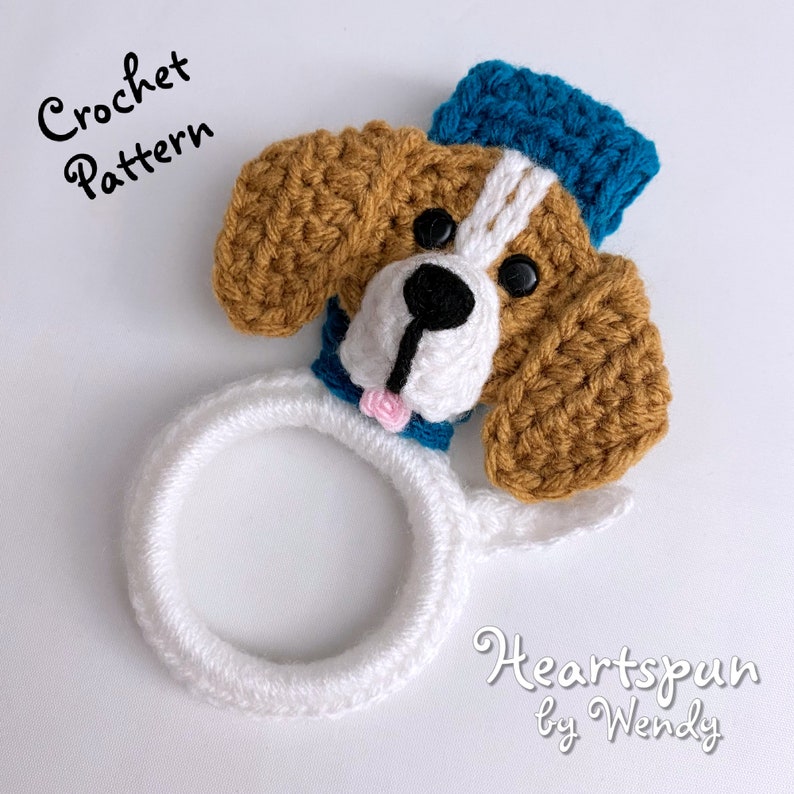 Puede incluir: Patr&oacute;n de crochet para un adorable juguete amigurumi en forma de perro con un sombrero azul. El perro es marr&oacute;n y blanco con un anillo blanco alrededor del cuello. El patr&oacute;n se llama "Heartspun by Wendy".