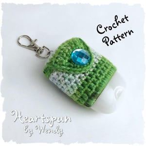 May include: Crochet pattern for a green and white hand sanitizer holder with a blue gem. The holder has a silver keychain attached. The text "Heartspun by Wendy" is written below the image.