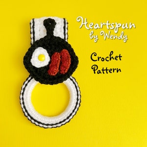 May include: Crochet pattern for a white and black dish towel ring with a black and red crocheted fried egg and sausage design on top. The pattern is called "Heartspun by Wendy".