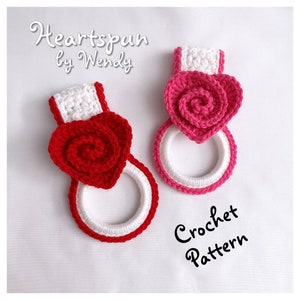May include: Two crocheted towel rings with heart-shaped rose embellishments. The rings are white with a red or pink border. The text "Heartspun by Wendy" and "Crochet Pattern" are visible.