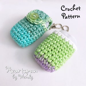 May include: Two crocheted hand sanitizer bottle holders. One is green and white with a purple bottom. The other is blue and green with a green button. Both have a silver keychain attached. Crochet Pattern Heartspun by Wendy.