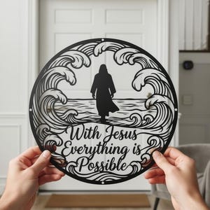 Könnte beinhalten: Ein kreisförmiges Wandkunstobjekt aus schwarzem Metall mit der Silhouette einer Figur vor Meereswellen. Der Text "With Jesus Everything is Possible" ist in einer Schreibschrift am unteren Rand des Motivs innerhalb des Rahmens eingearbeitet.