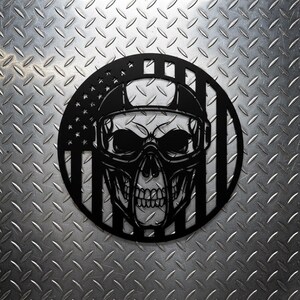 Könnte beinhalten: Schwarze Metall-Wandkunst mit einem Totenkopf, der einen Helm und eine Brille trägt, vor dem Hintergrund der amerikanischen Flagge. Das kreisförmige Design zeigt detailliert die Merkmale des Schädels.