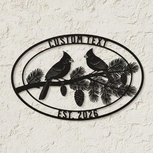 Könnte beinhalten: Schwarze Metall-Wandkunst mit zwei Vögeln auf einem Ast mit Kiefernnadeln und Zapfen. Das ovale Design enthält den Text "CUSTOM TEXT" und "EST. 2026", ideal für personalisierte Heimdekoration. Geeignet für den Innen- und Außenbereich.