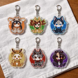 May include: Six clear acrylic keyrings featuring cartoon characters in animal costumes. Each keyring has a silver-coloured metal ring. The characters are in various colours, including orange, green, blue, yellow, red, and purple.