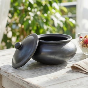 May include: A black ceramic pot with a lid, next to a glass bowl of granola and berries. A spoon rests on a linen napkin. The words "SLOW LIVING" are printed at the bottom of the image.