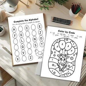 May include: Two activity sheets for children. One sheet is titled "Complete the Alphabet" and features letter blanks. The other sheet is titled "Color by Code" and has a cow graphic with balloons. Pencils and other desk items are in the background.