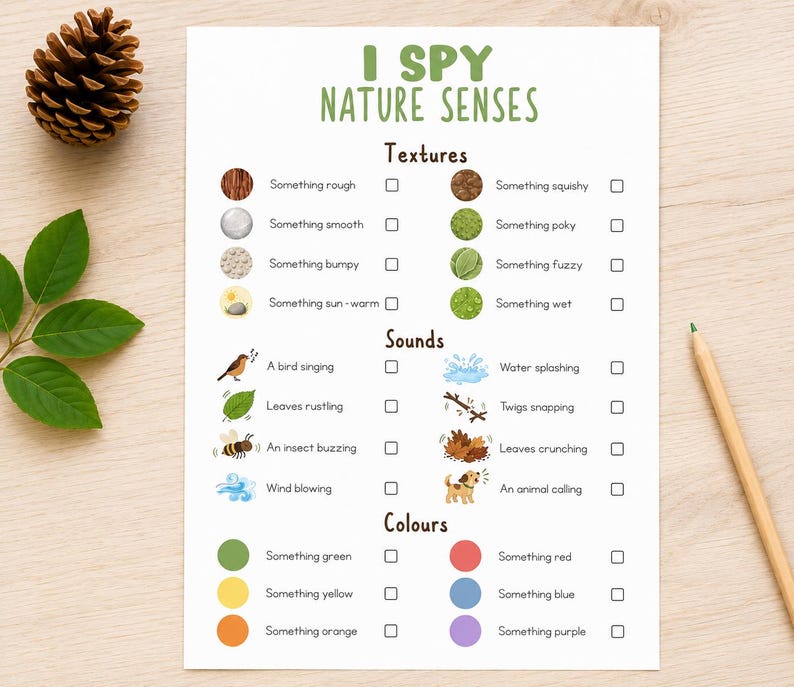 May include: A printed "I Spy Nature Senses" activity sheet with illustrations and check boxes. The sheet includes categories for textures, sounds, and colors. A pinecone, leaves, and a pencil are on the wooden surface.
