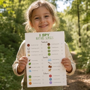 May include: A young girl smiles while holding a white paper with the text "I SPY NATURE SENSES". The paper lists textures, sounds, and colors to identify in nature. The background is a blurred forest scene.