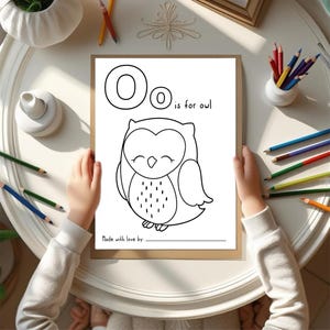 May include: A coloring page with the letter "O" and the phrase "is for owl" above a cartoon owl illustration. The page is held by hands, surrounded by colored pencils and art supplies.