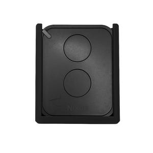 Peut inclure: Accessoire noir pour appareil photo Nikon, avec deux boutons circulaires et le nom de la marque imprimé en bas. Le dispositif rectangulaire a un bord surélevé et une petite languette en haut.