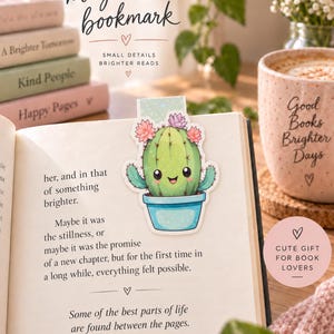 May include: A magnetic bookmark featuring a green cartoon cactus with a smiling face, pink and purple flowers, and a blue pot. The bookmark is clipped onto an open book page. Text on the image reads magnetic bookmark, small details brighter reads.
