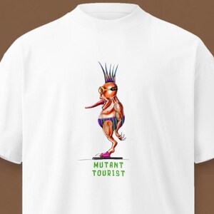 Könnte beinhalten: Ein weißes T-Shirt mit kurzen Ärmeln und einer Grafik einer Cartoon-Kreatur mit Irokesenschnitt, Schutzbrille und langer Zunge, die eine gestreifte Badehose trägt. Die Kreatur steht auf einer Plattform über dem grünen Text MUTANT TOURIST.