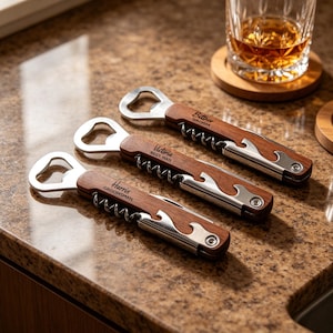 Puede incluir: Tres abridores de botellas de madera personalizados con detalles de acero inoxidable. Cada abridor tiene un sacacorchos, un abridor de botellas y un cuchillo pequeño. Los nombres "Harris, Groomsman", "Victoria, Best Man" y "Bottner, Groom" están grabados en la madera.