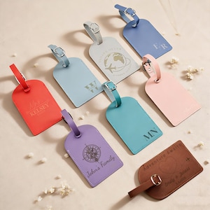 Puede incluir: Una colección de etiquetas de equipaje personalizadas en varios colores, incluyendo rojo, azul y rosa. Algunas etiquetas presentan iniciales, nombres o diseños temáticos de viajes. Las etiquetas están hechas de material similar al cuero y tienen hebillas y correas.