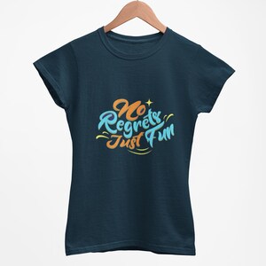 Puede incluir: Una camiseta azul marino con la frase "No Regrets Just Fun" en una fuente colorida y estilizada. El texto está en tonos de azul, naranja y amarillo. La camiseta está colgada de una percha de madera.