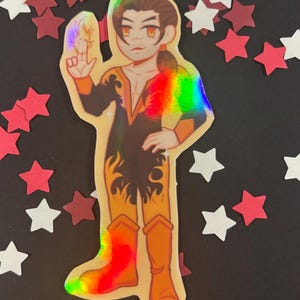 May include: Holographic sticker featuring a cartoon character in a black and orange outfit with flames. The character is wearing orange boots and has a rainbow effect on the chest and boots. The background is black with red and white star-shaped confetti.