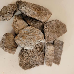 May include: A cluster of irregularly shaped, rough-textured rocks in shades of grey and brown. The stones have a porous appearance, with visible patterns and colour variations. The arrangement suggests a natural, organic theme.