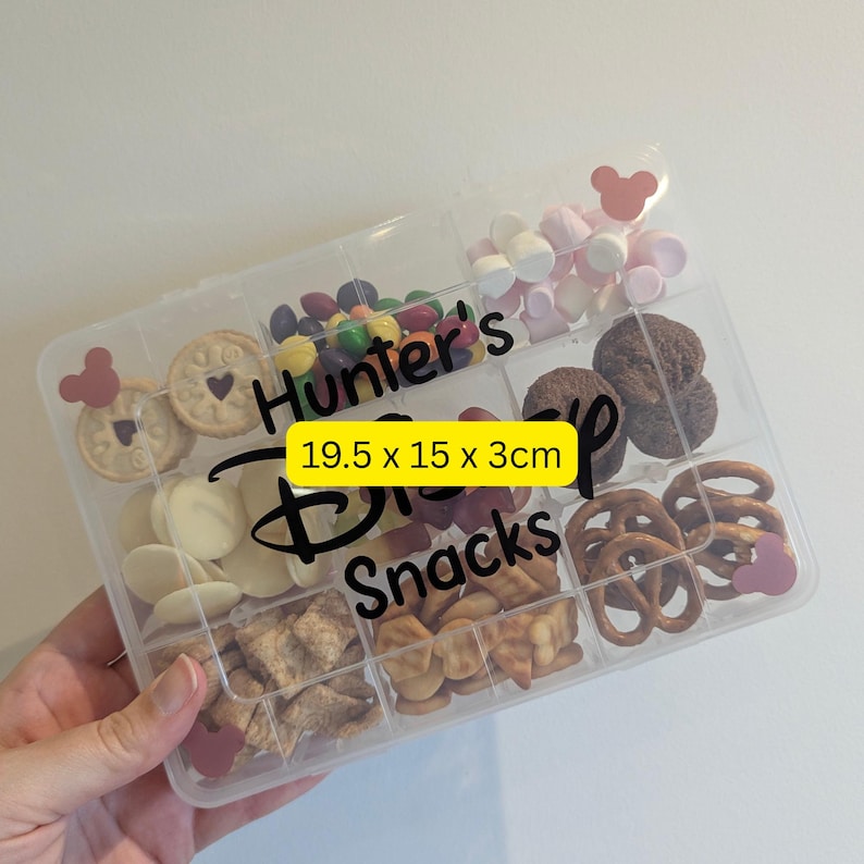 May include: A clear plastic snack box with multiple compartments filled with various treats, including cookies, candies, and pretzels. The box is labeled "Hunter's Disney Snacks" and measures 19.5 x 15 x 3cm.