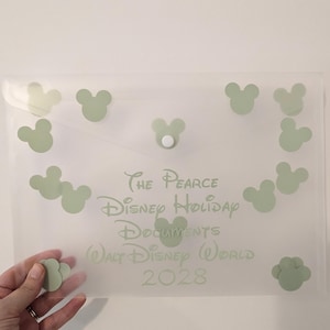 May include: A transparent document holder with a white press stud closure. It features light green Mickey Mouse head shapes and text reading "The Pearce Disney Holiday Documents Walt Disney World 2028."