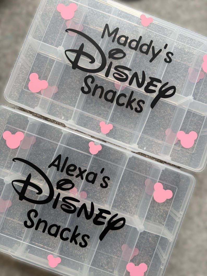 May include: Two clear plastic snack organizers with multiple compartments. Each organizer has the words "Maddy's Disney Snacks" and "Alexa's Disney Snacks" in black script, along with pink Mickey Mouse head accents.