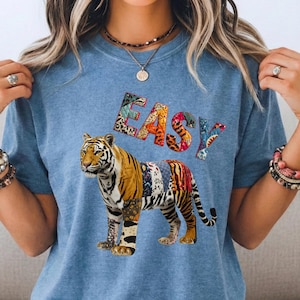May include: A blue jean-coloured t-shirt with a tiger design. The tiger is made up of patchwork patterns and the word "EASY" is in colourful letters. The tiger's body is a mix of textures and colours. This is a casual wear item.